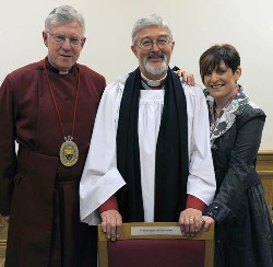 Canon Budd pictured with his wife Carla in the Chapter Room of Lisburn Cathedral at the chair bearing his new title ‘Prebendary of Rasharkin’.  With them is Dean John Bond.